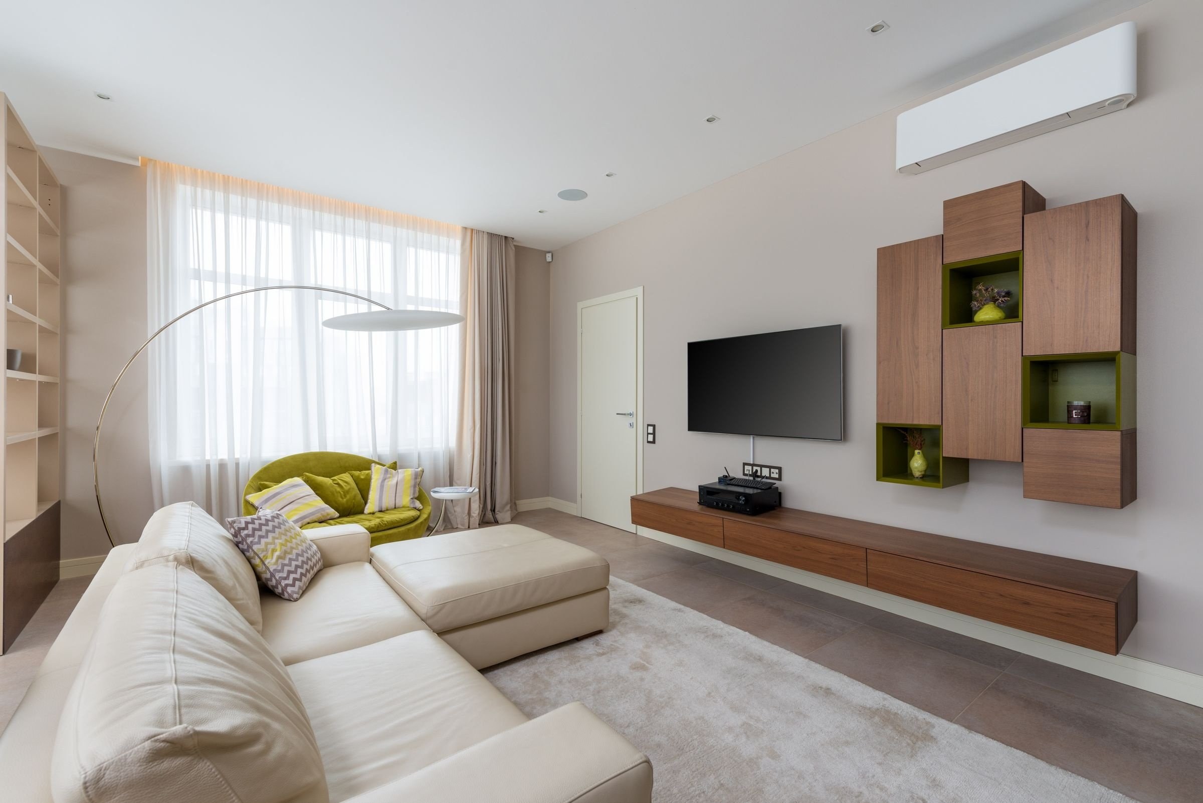 Helles Wohnzimmer mit beigem Ecksofa, Holz-Wandregal und weißem Klimaanlagen-Innengerät hoch an der Wand